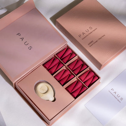 Open pink box with dark pink incense cones and a white incense burner, branded 'PAUS', on a light background.