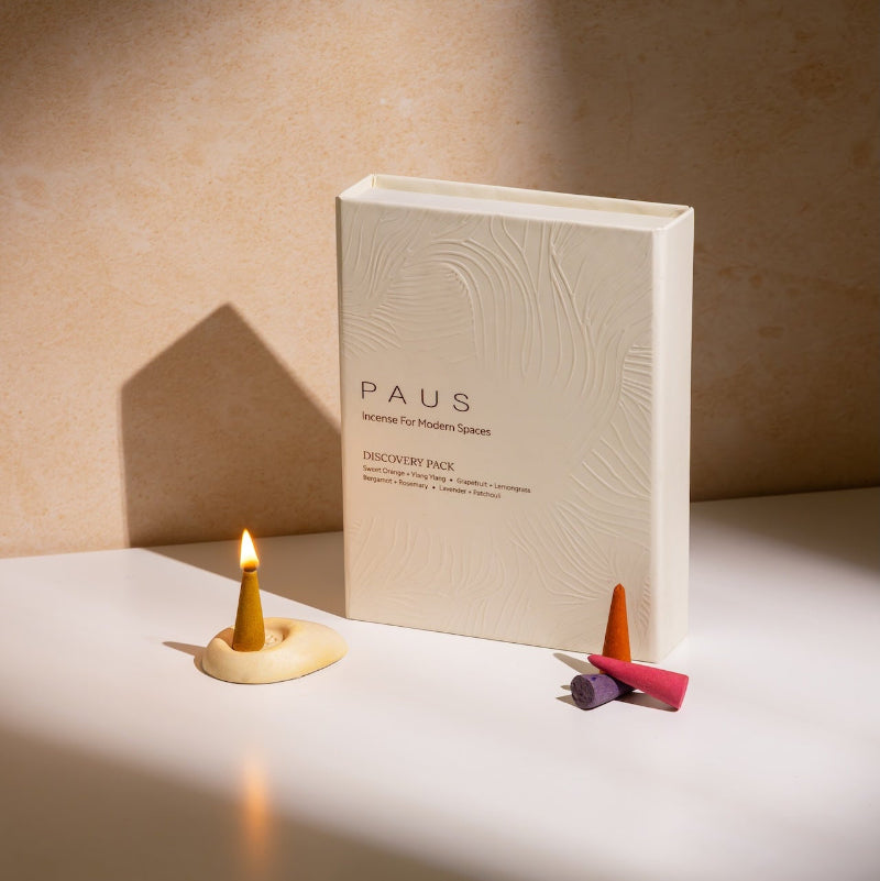 PAUS mood-enhancing incense product packaging on a beige surface with incense lit up